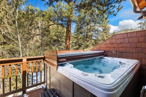 A hot tub on a deck with a wooden railing, surrounded by trees. - Riverfront Hideaway • Private Hot Tub • Near RMNP (Estes Park)