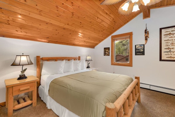 A bedroom with a wooden ceiling, a bed with white bedding, a nightstand with a lamp, and a framed fish illustration on the wall. - Quiet Fall River Escape • Riverside • RMNP (Estes Park)