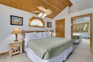 A bedroom with a bed, wooden headboard, bedside tables with lamps, a ceiling fan, and a large mirror.