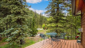 Une terrasse en bois avec une table et des chaises, entourée d’une forêt dense.