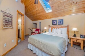 Une chambre à coucher avec un grand lit, un plafond en bois, une lucarne et une tapisserie murale.