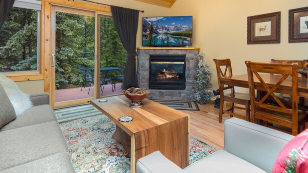 Un salon chaleureux avec une cheminée, des meubles en bois et une grande fenêtre donnant sur une forêt.