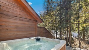 Una cabaña de madera con un jacuzzi en un área boscosa.
