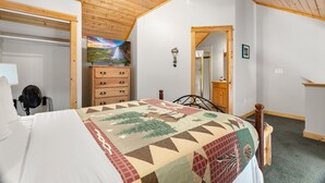 Un dormitorio con techo de madera, una cama con colcha, un aparador, un televisor y un espejo.