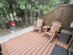 Une terrasse en bois avec deux fauteuils Adirondack et un barbecue.