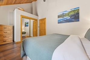 Une chambre à coucher avec un lit, une commode, un miroir et un tableau accroché au mur.