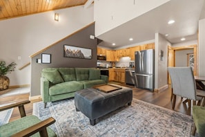 A modern living room with a green sofa, a black ottoman, and a patterned rug. - Fall River Hideaway • Private Hot Tub • Near RMNP (Estes Park)