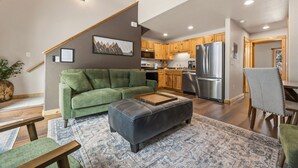 A modern living room with a green sofa, a black ottoman, and a patterned rug. - Fall River Hideaway • Private Hot Tub • Close to RMNP (Estes Park)