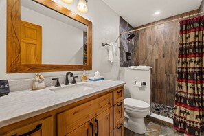 A bathroom with a wooden vanity, a large mirror, a white toilet, and a shower area with a patterned curtain.