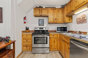 A kitchen with wooden cabinets, a stainless steel oven, a microwave, and a fire extinguisher. - Riverfront Retreat • Private Hot Tub • Near RMNP (Estes Park)