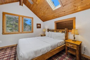 A bedroom with a wooden bed, two windows, a mirror, a bedside table with a lamp, and a plaid floor.