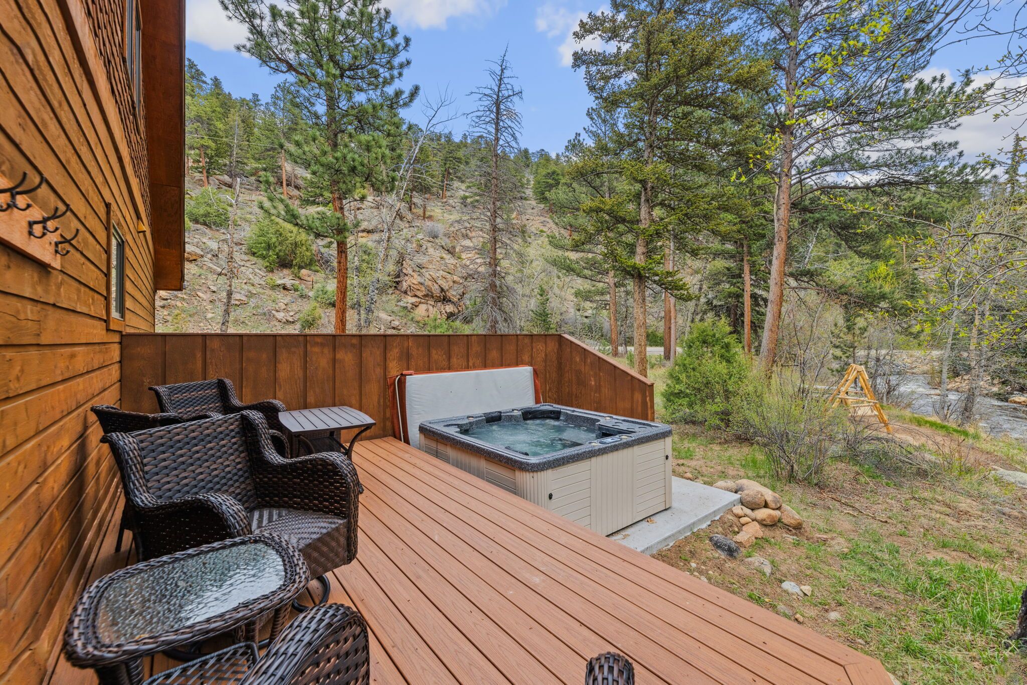 A wooden deck with wicker furniture and a hot tub, surrounded by a forested hillside.