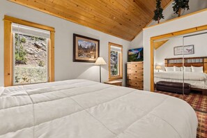 Een slaapkamer met een groot bed, houten plafond en uitzicht op een rotsachtig landschap door het raam.