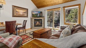 Un salon chaleureux avec une cheminée, un plafond en bois, de grandes fenêtres et un canapé confortable.