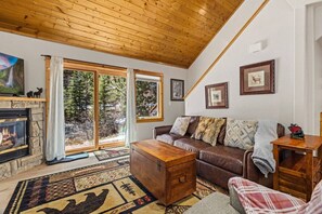 A cozy living room with a fireplace, a sofa, a coffee table, and a view of the outdoors. - Riverfront Retreat • Private Hot Tub • Near RMNP (Estes Park)