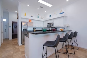 A modern kitchen with white cabinets, a central island with bar stools, a refrigerator, and a microwave. - Beachfront Townhouse(24) Pet Friendly Covered Deck (Panama City Beach)