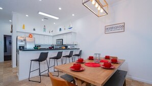 Una cocina moderna con armarios blancos, una isla central con taburetes altos y una mesa de comedor para cuatro personas, con vajilla roja.