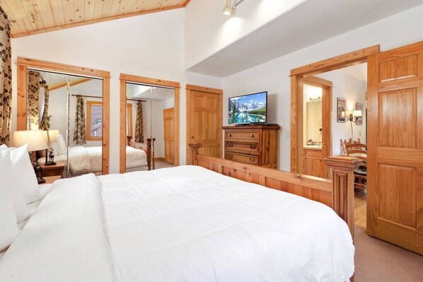 A hotel room with a large bed, wooden furniture, a television, and a mirror.