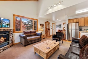 A spacious living room with a fireplace, a large window with a mountain view, a dining area, and a kitchen with modern appliances.