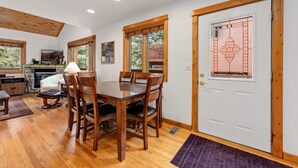 Un coin repas comprenant une table et des chaises en bois, une cheminée et une porte agrémentée d’un panneau de verre décoratif.