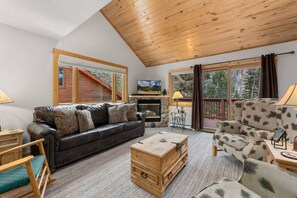 A cozy living room with a fireplace, a sofa, a coffee table, and a view of the outdoors.