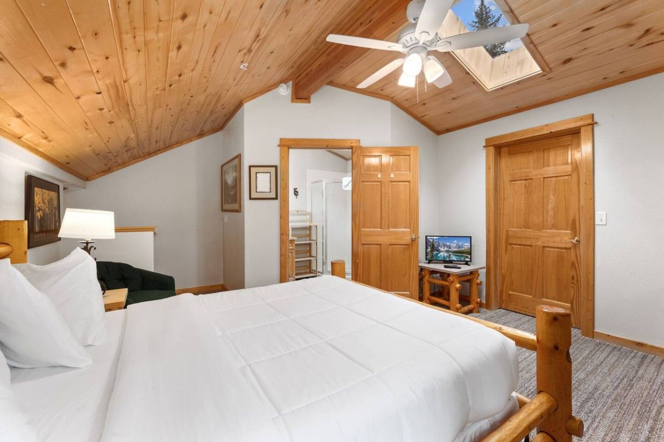 Ein Hotelzimmer mit Holzbalkendecke, einem Bett mit weißer Bettwäsche, einem Fernseher auf einem Holzständer und zwei Holztüren.