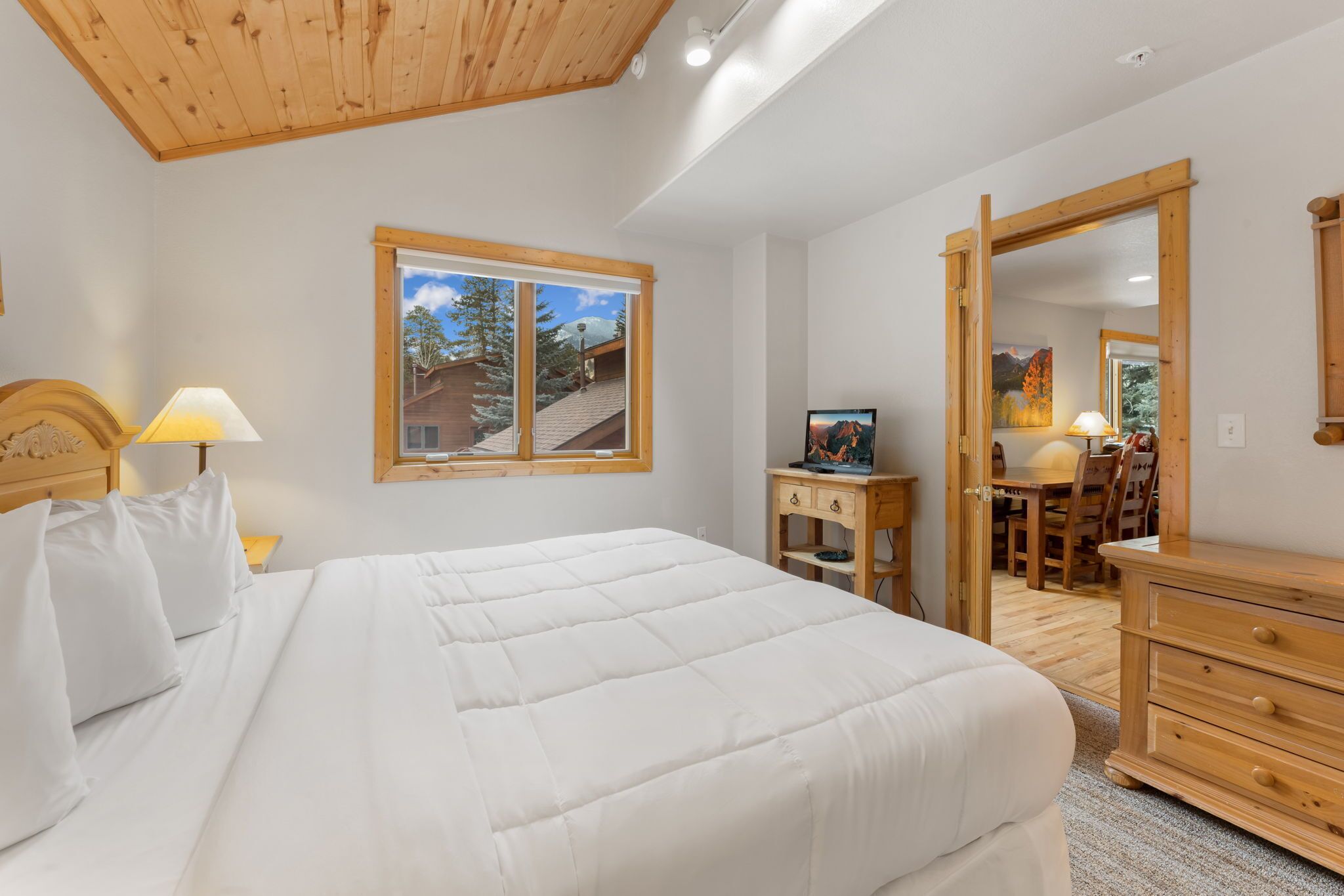 Un dormitorio con una cama grande, cabecera de madera, una mesita de noche con lámpara, cómoda de madera, escritorio con silla y un espejo grande.