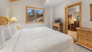 A bedroom with a large bed, wooden headboard, a nightstand with a lamp, a wooden dresser, a desk with a chair, and a large mirror. - Fall River Retreat • Mountain Views • RMNP (Estes Park)