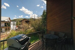 Un balcon avec un barbecue, des chaises et une vue sur une maison et des arbres.