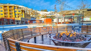 Una plaza pública con un área circular de bancos de madera y un brasero en el centro.
