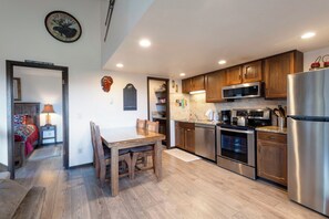 A modern kitchen with wooden cabinets, stainless steel appliances, and a dining area with a wooden table and chairs.