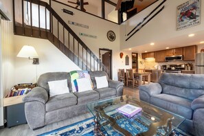 Un vaste espace de vie comprenant deux canapés gris, une table basse en verre et un escalier menant à un niveau supérieur.