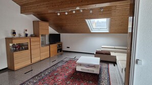 Un salon moderne avec un plafond en bois, un téléviseur, un canapé, une table basse et un tapis à motifs.