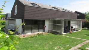 Une maison moderne dotée d’un toit en pente, de grandes fenêtres et d’un porche abrité.