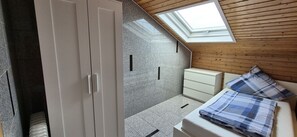 Ein Schlafzimmer mit Dachfenster, einem Kleiderschrank, einem Bett mit Karo-Bettwäsche und einem kleinen Nachttisch.