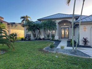 Stunning home with a symmetrical facade, surrounded by lush gardens and tropical plants.
