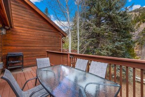 Une cabane en bois avec une table et des chaises en verre sur une terrasse, entourée d’arbres.