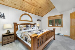 Ein Schlafzimmer mit einem hölzernen Bett, zwei Nachttischen, einem Fenster mit Blick auf Bäume und einer Holzbalkendecke.