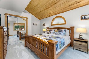 A bedroom with a wooden bed, a nightstand, a mirror, and a window with a view of trees.