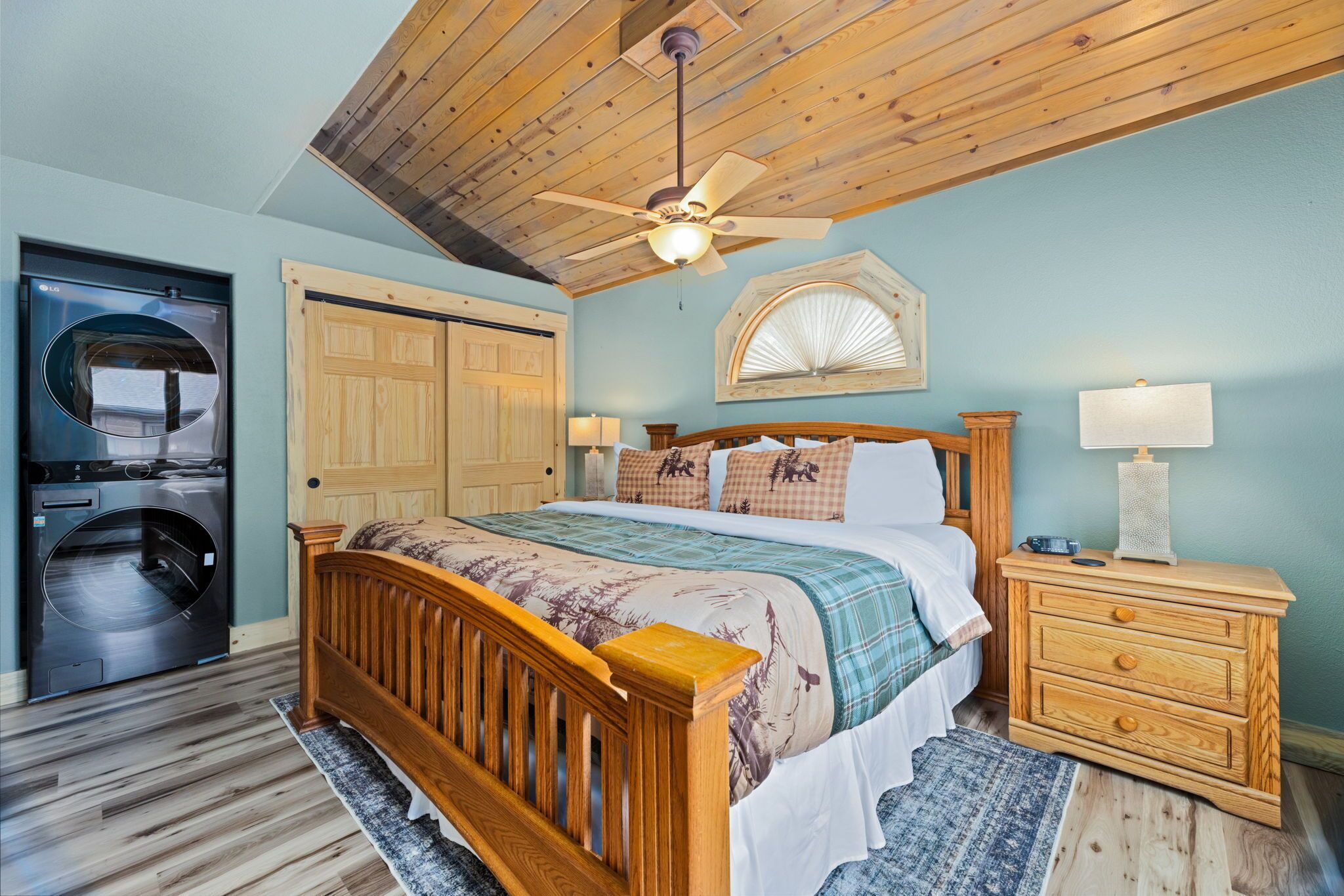 A bedroom with a wooden bed, a ceiling fan, a washing machine, and a wooden dresser.