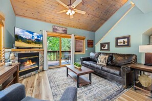 A cozy living room with a fireplace, a leather couch, a television, and a view of the outdoors. - Riverfront Escape • A/C • Near RMNP (Estes Park)