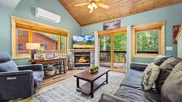 A cozy living room with a fireplace, comfortable seating, and large windows offering a view of the outdoors.