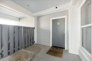 Une entrée d’habitation avec une porte grise, une boîte aux lettres et un sol en béton.