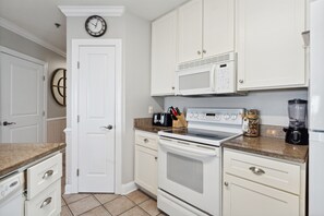 Una cocina con armarios blancos, un microondas, una estufa y un reloj en la pared.