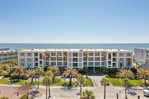 Un hôtel à plusieurs étages offrant une vue sur la plage, doté d’une cour intérieure avec des palmiers et d’un espace de stationnement.