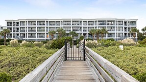 A multi-story hotel with balconies, a wooden boardwalk leading to the entrance, and a landscaped garden with various plants.