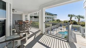 A covered outdoor deck with a pool, seating area, and a view of the ocean.