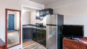 A compact kitchen with dark cabinets, a stainless steel refrigerator, a microwave, and a flat-screen TV on a wooden cabinet.