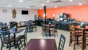 A restaurant with multiple tables and chairs, a kitchen area, and a bright orange accent wall.