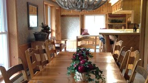 A wooden dining table with chairs, a chandelier, and a Christmas tree centerpiece.